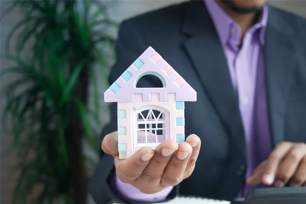 Person holding a model house while working out home insurance cost on a calculator